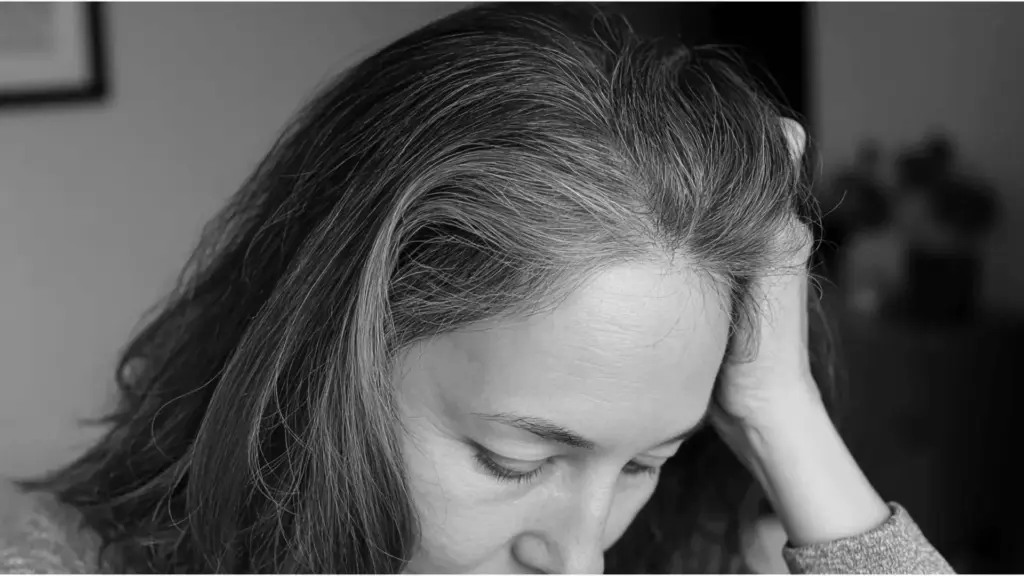 Close-up of a woman with visible gray roots and thinning hair at her part line, illustrating concerns about hrt and hair loss copy