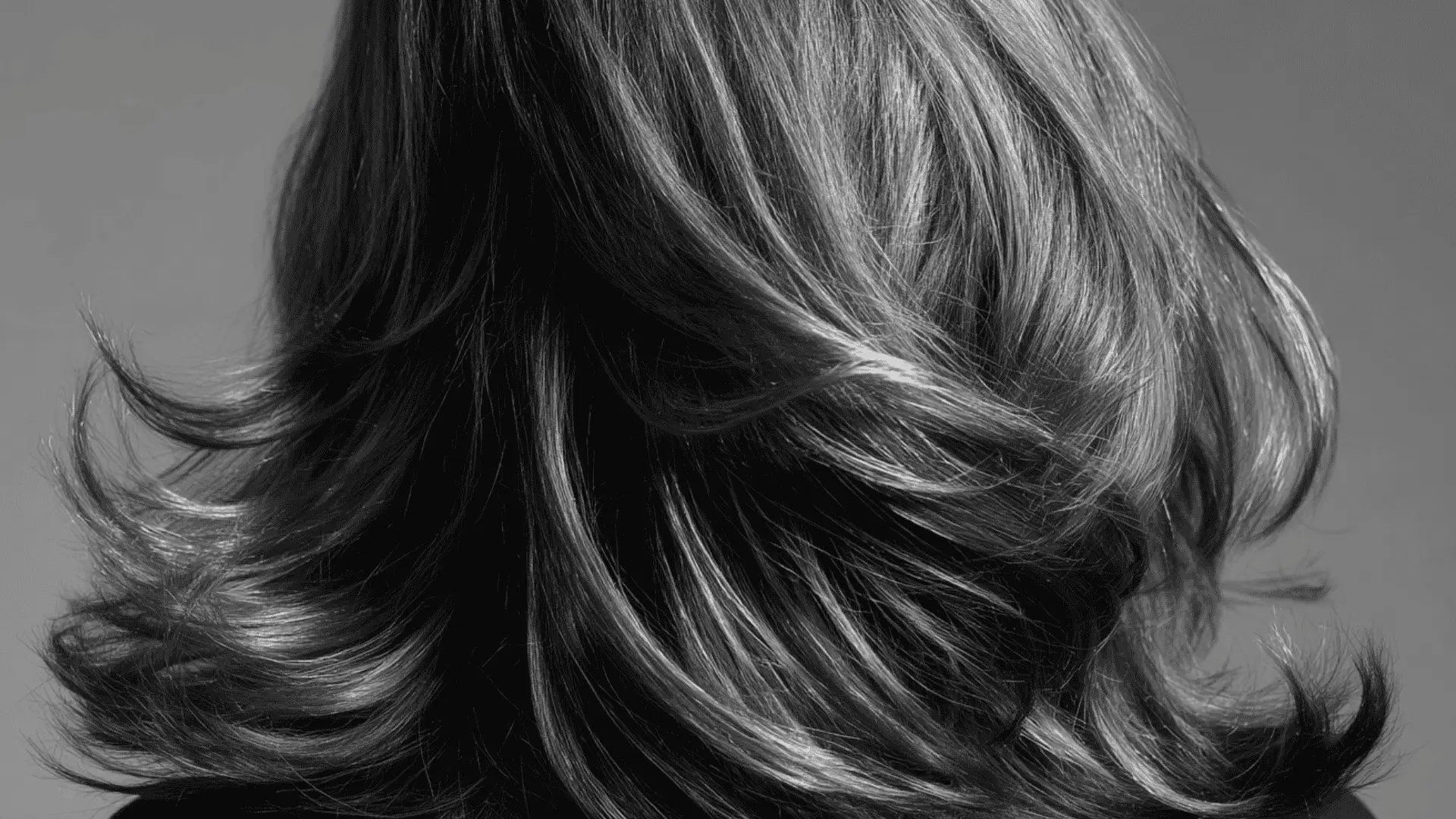 A view of a long straight dark grey formal hairstyle demonstrating how to make hair look fuller in a sleek and polished manner