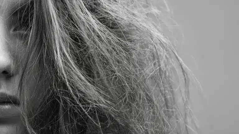 A woman with curly, frizzy hair due to leave-in conditioner gazes at her reflection in the mirror.