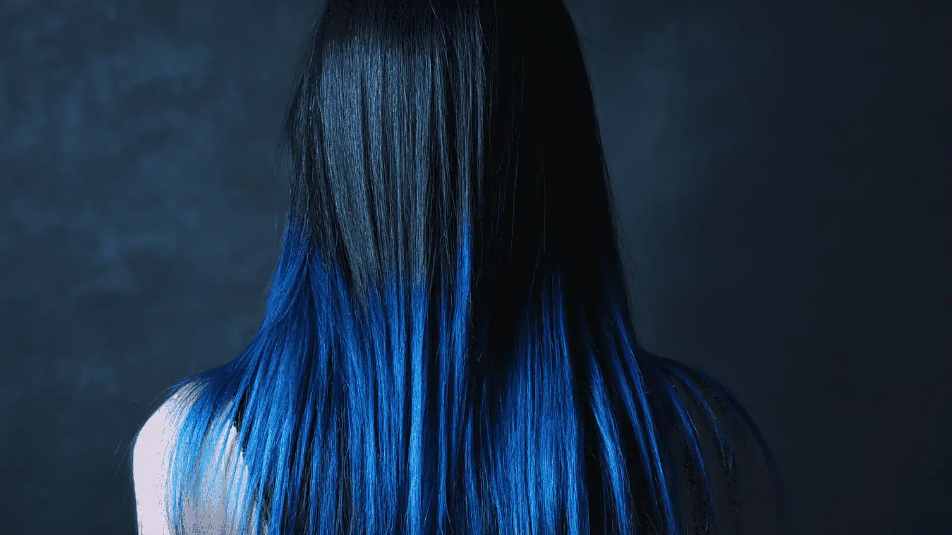 A woman with long black hair featuring a vibrant blue dip-dye at the ends showcasing a trendy hair coloring technique
