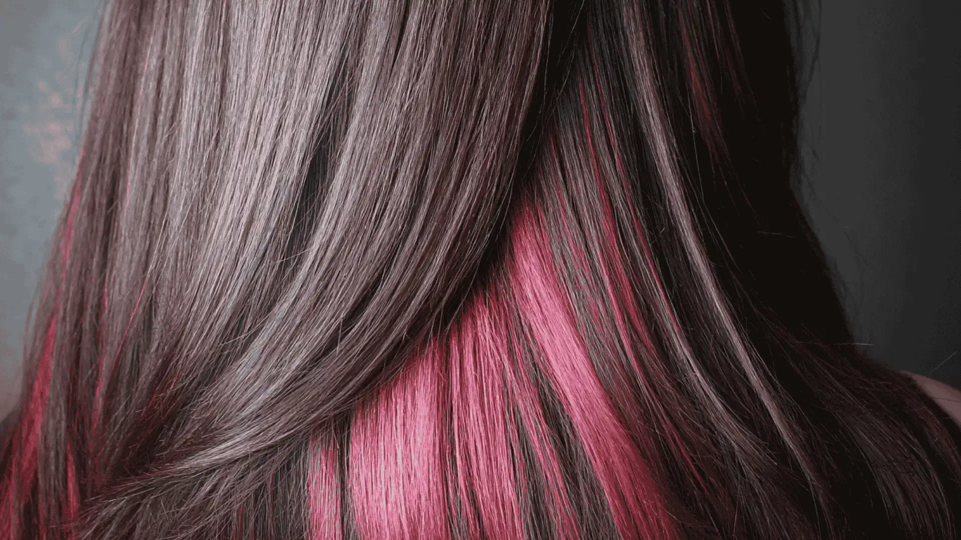A woman with long dark hair accented by pink highlights styled with the Peek-a-boo Underlights hair coloring technique