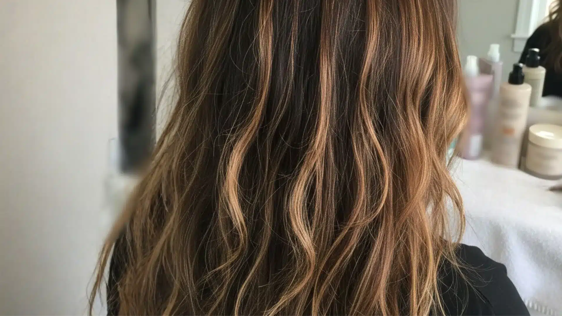 A woman with long, wavy hair considers switching from balayage back to her natural hair color