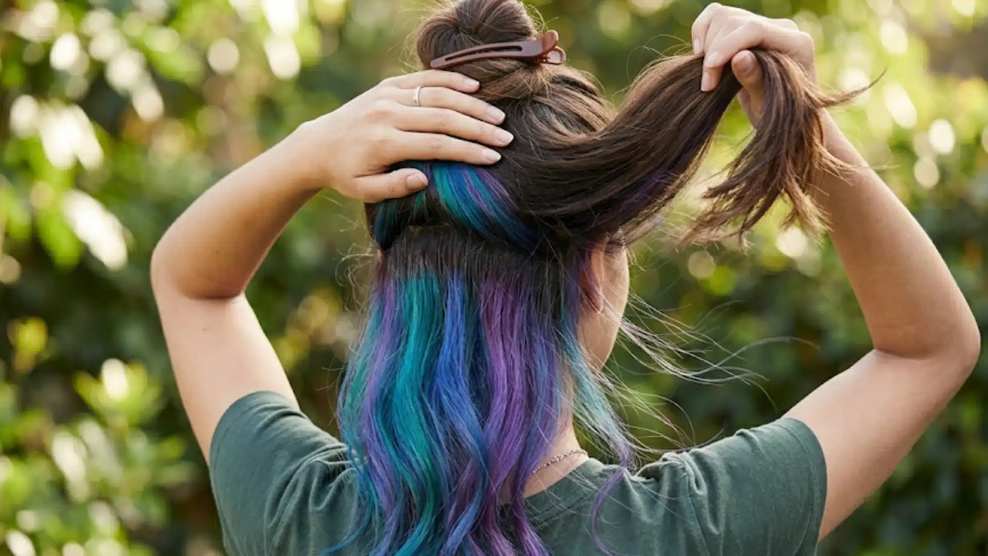 Back view of woman lifting hair to reveal vibrant peekaboo colors, showing underdye hair upkeep and care in natural outdoor light