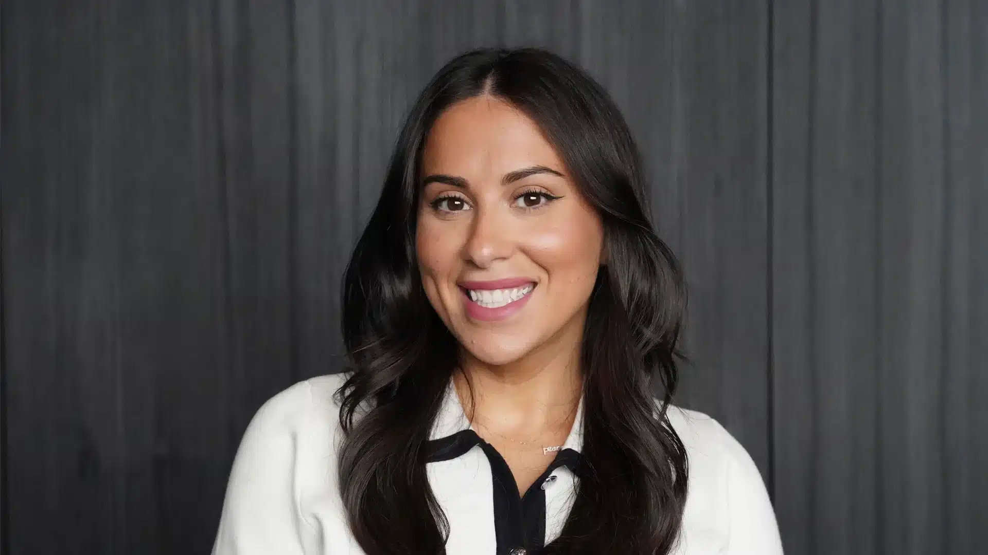 Claudia Oshry featuring her long healthy black hair dressed in a white shirt exuding poise