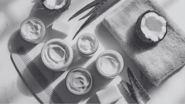Flat lay of natural hair care cream jars, coconut, aloe, soap bars, wooden comb on white marble
