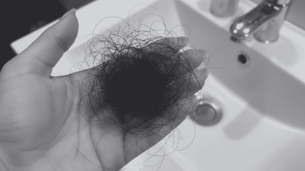 Hand holding a clump of dark, loose hair over a white bathroom sink.