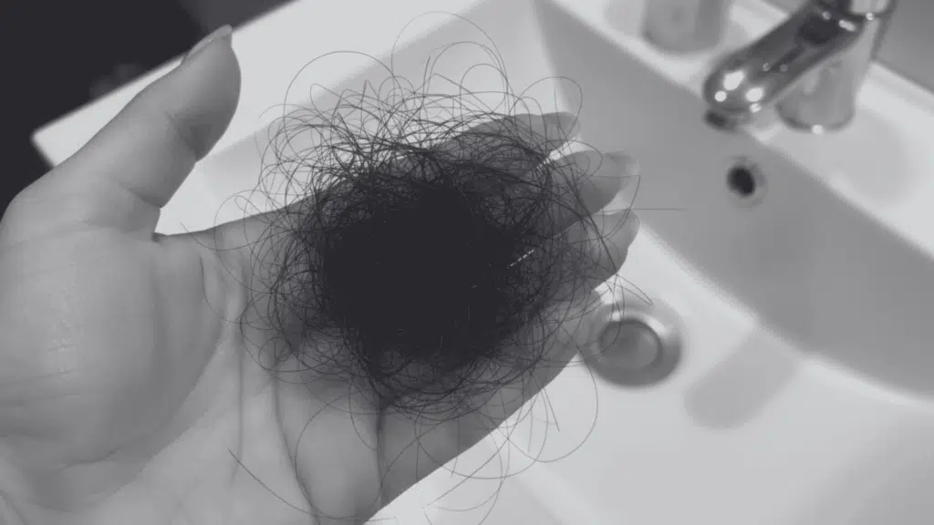 Hand holding a clump of dark, loose hair over a white bathroom sink.