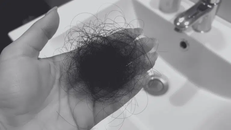 Hand holding a clump of dark, loose hair over a white bathroom sink.