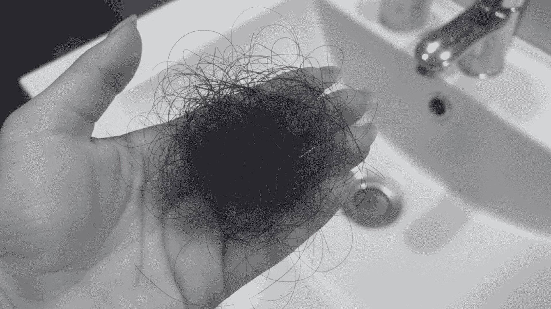 Hand holding a clump of dark, loose hair over a white bathroom sink.