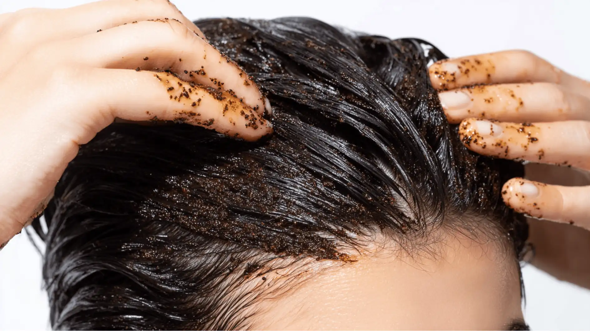 Hands applying a scalp scrub in sections with fingertips focusing on skin beneath hair to remove buildup before rinsing step