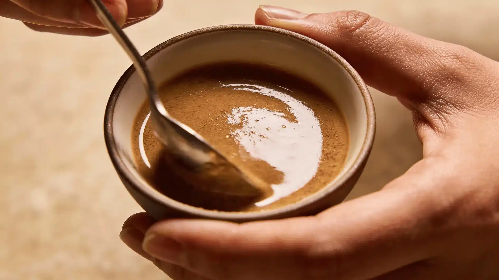 Hands mixing brown sugar and oil in a small bowl to prepare a home scalp scrub before gentle massage and rinsing step