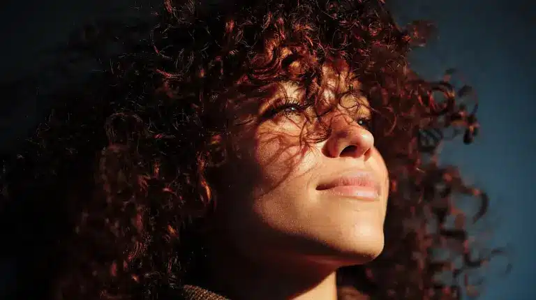 How Diet Changes Curly Hair Health and Growth Over Time shown in a close-up of a woman with dark auburn curls in dappled sunlight