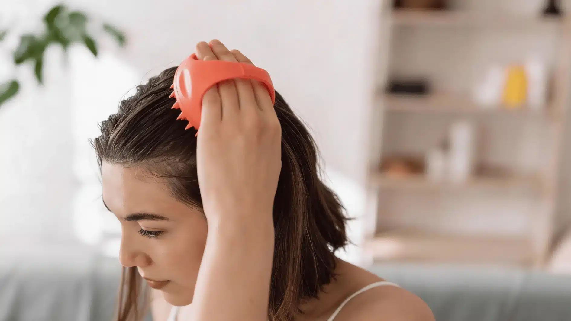 Woman demonstrating how to exfoliate scalp by gently massaging her head with fingertips in a bright bathroom setting