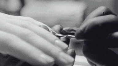 A close up black and white image showing a manicurist wearing black gloves applying a gel polish