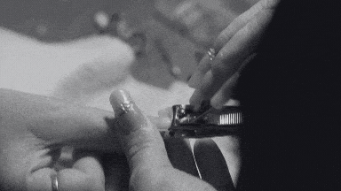 A close up black and white image showing a person using nail clippers to trim another perosn's nail