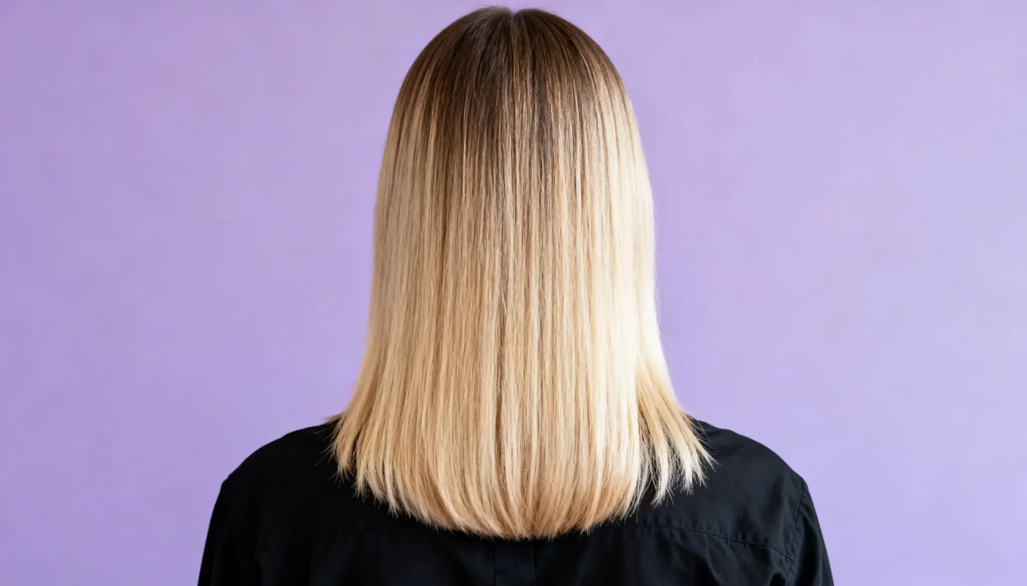 A person with straight, shoulder-length blonde hair is shown from the back, wearing a black shirt against a light purple background