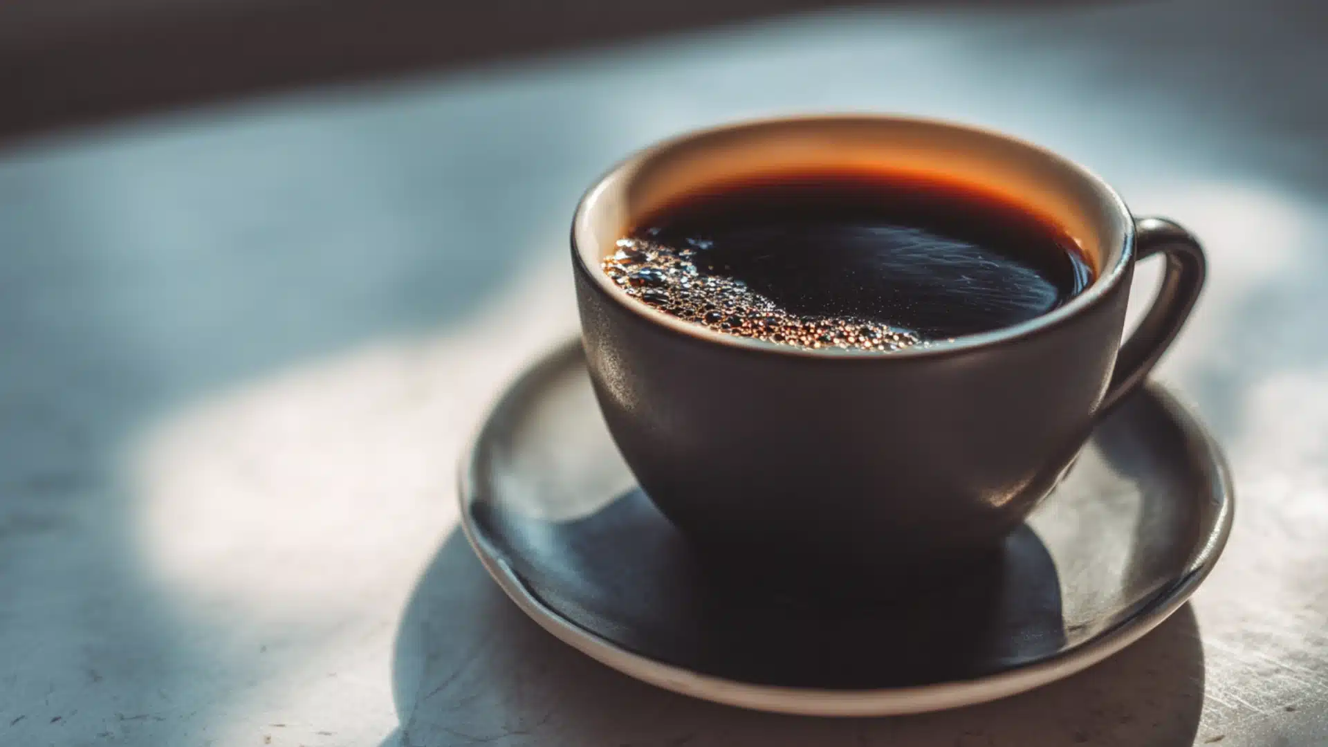 black textured mug filled with dark coffee and golden foam on a saucer calories in coffee shown in a close up side view (1)