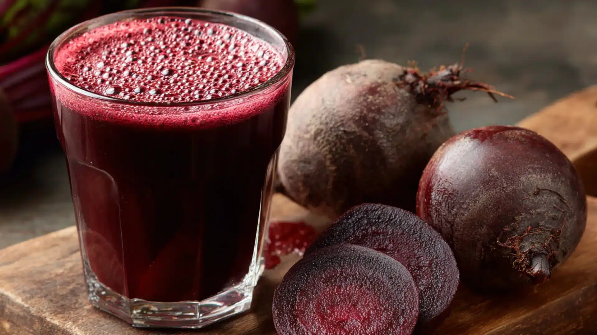 glass of deep red beetroot juice with bubbles in a tall cup next to sliced and whole beets on a rustic wooden board juice (1)