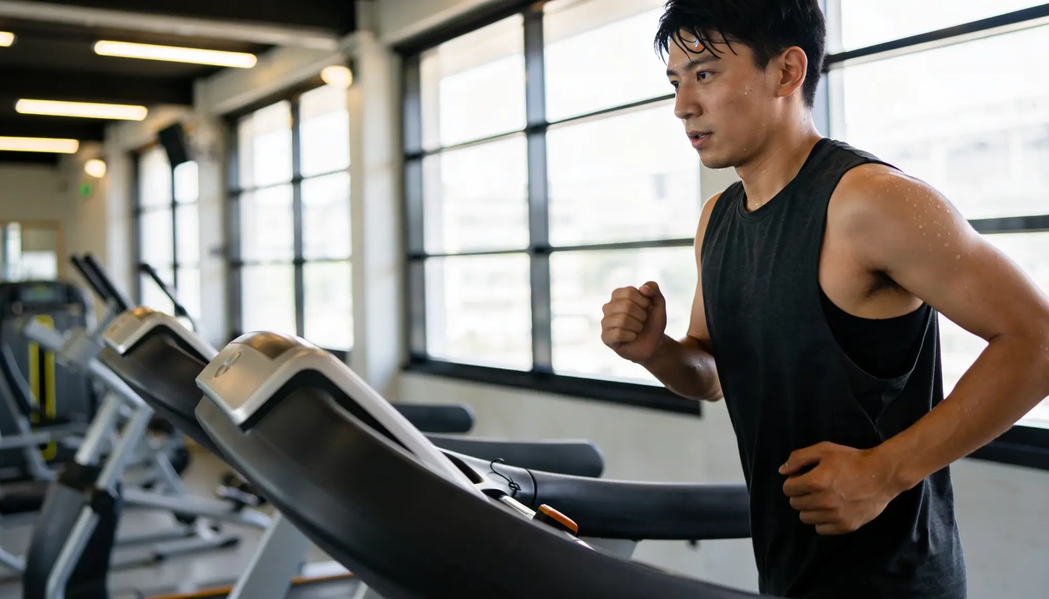 Person running on a treadmill at a steady pace in a gym with cardio machines and workout metrics visible in the background
