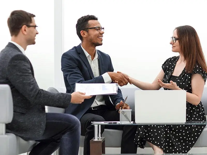 Business professionals shaking hands across a glass table in a modern office setting