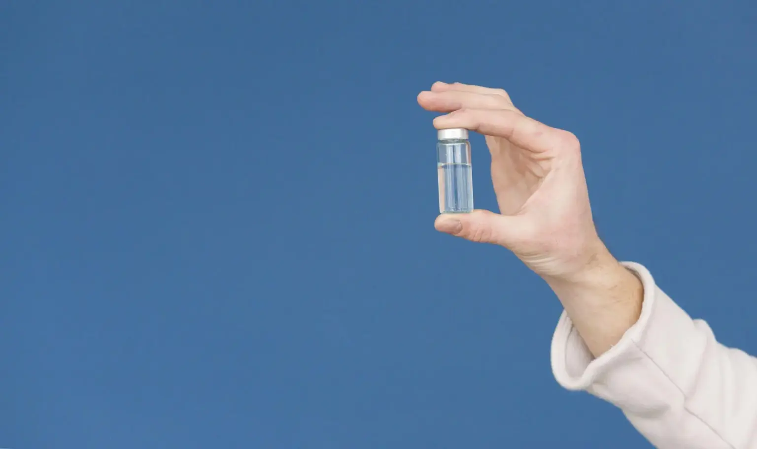 Hand holding small glass vial against blue background