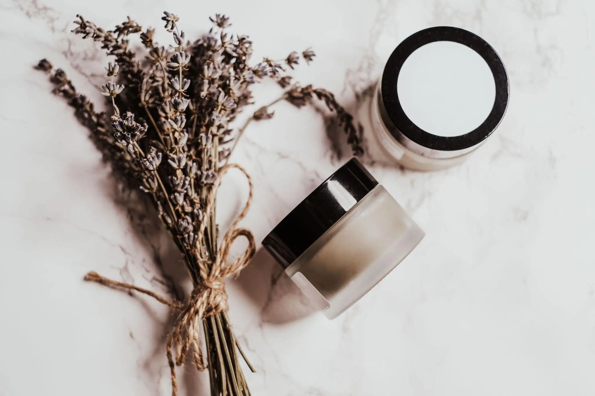 Dried lavender bouquet and skincare jars on marble surface in soft lighting