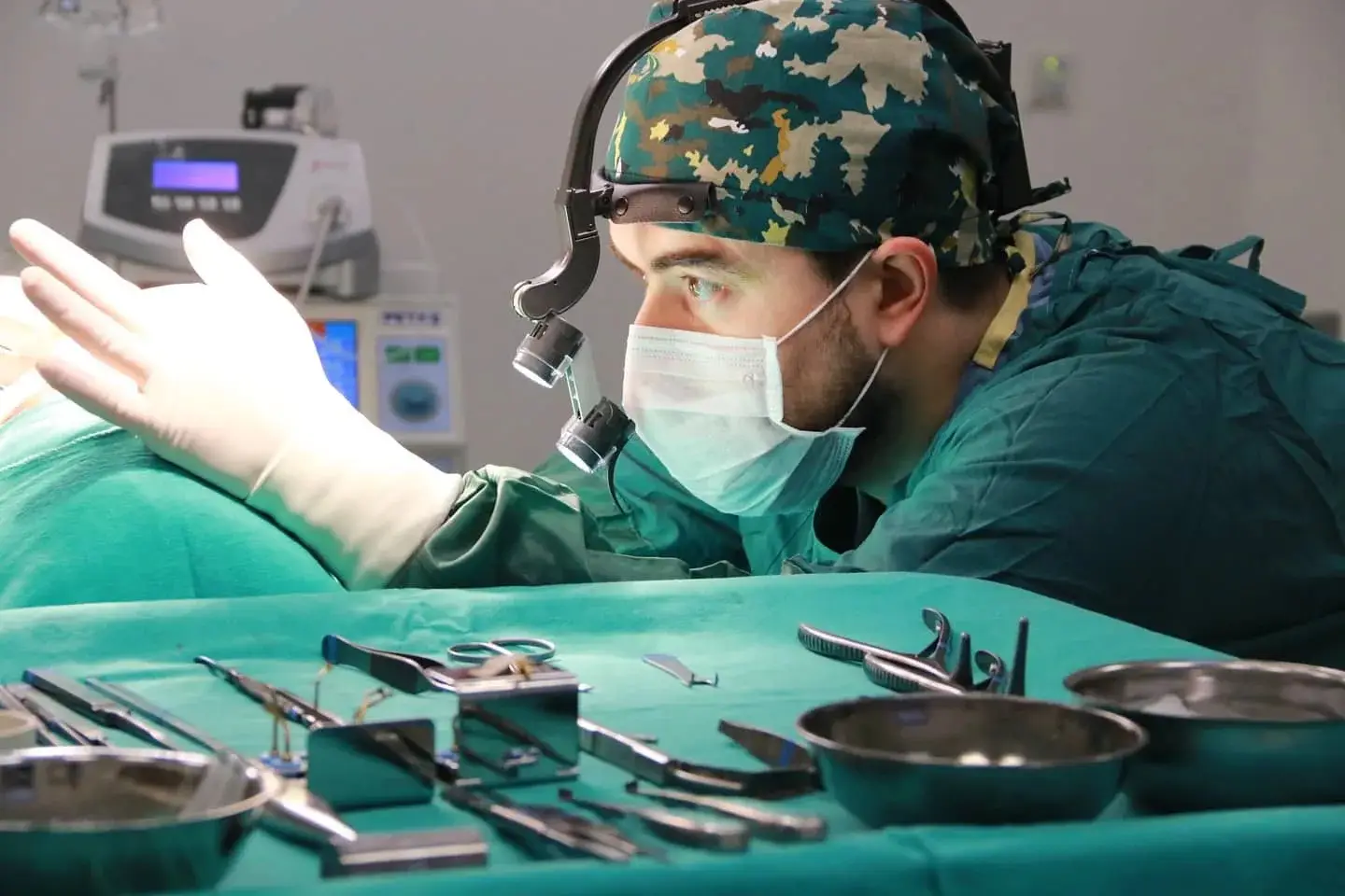 Surgeon in green scrubs performing surgery with tools laid out on table