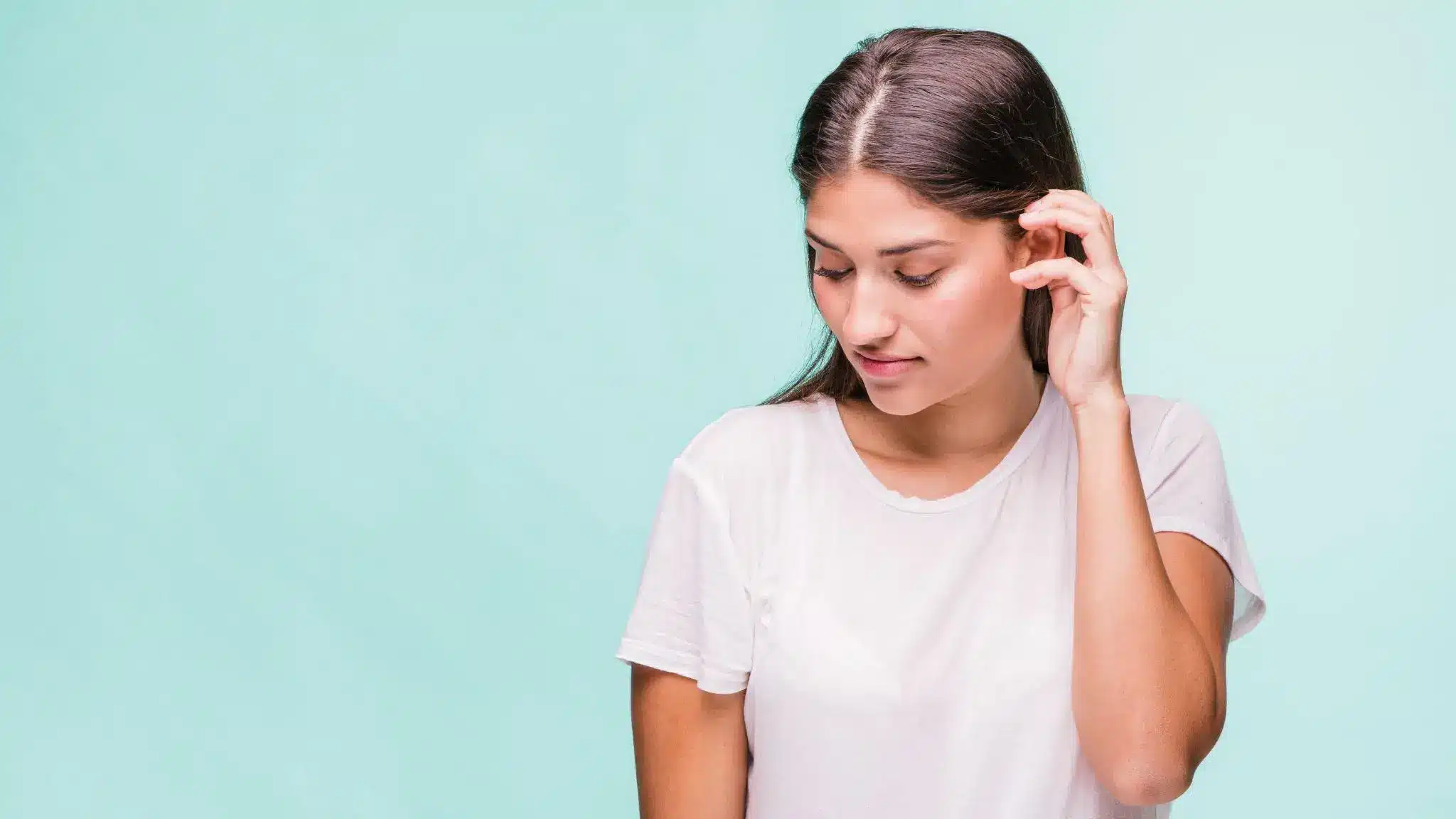 Woman in white shirt touching hair against light blue background