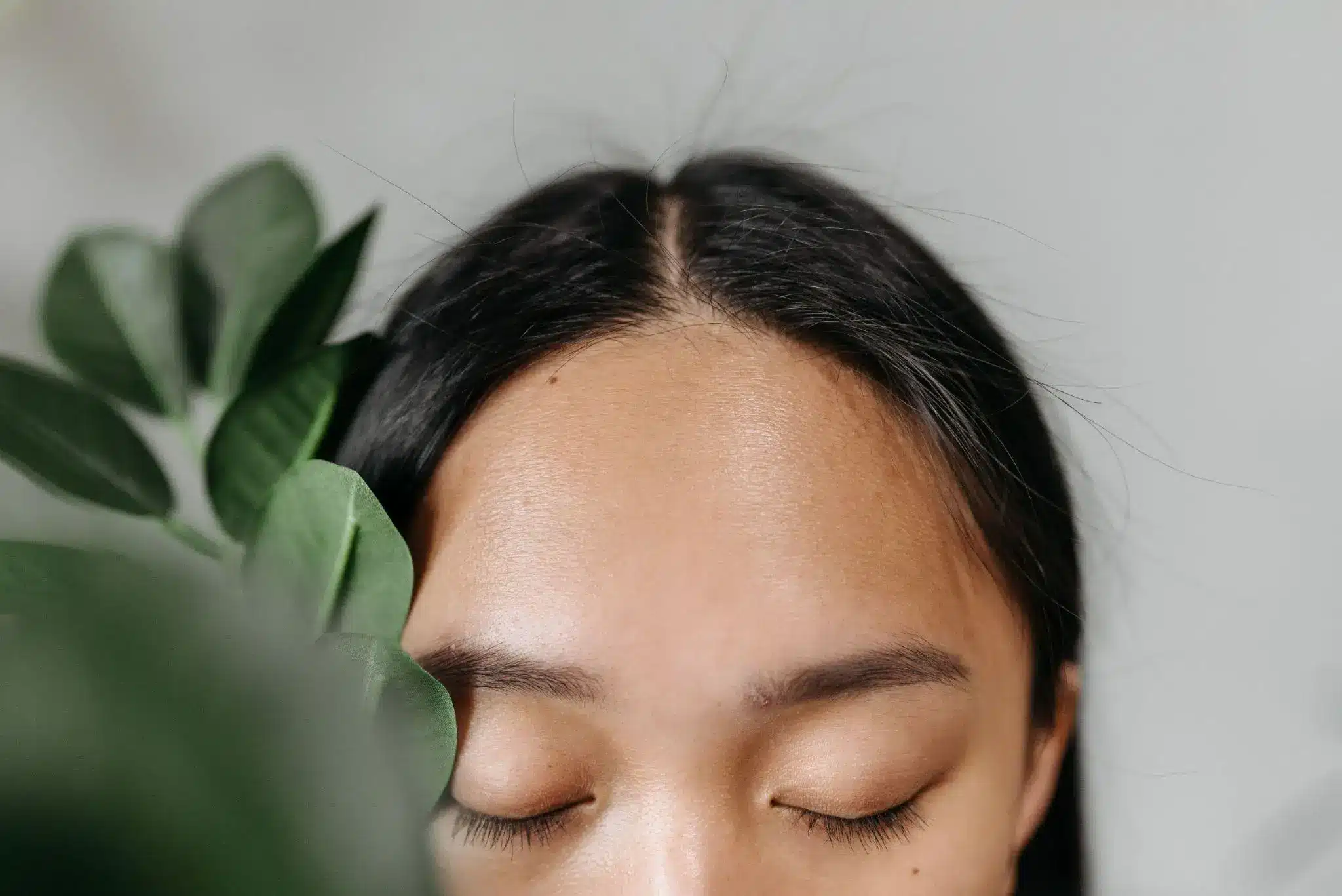 Close-up of a person with closed eyes next to green leaves indoors