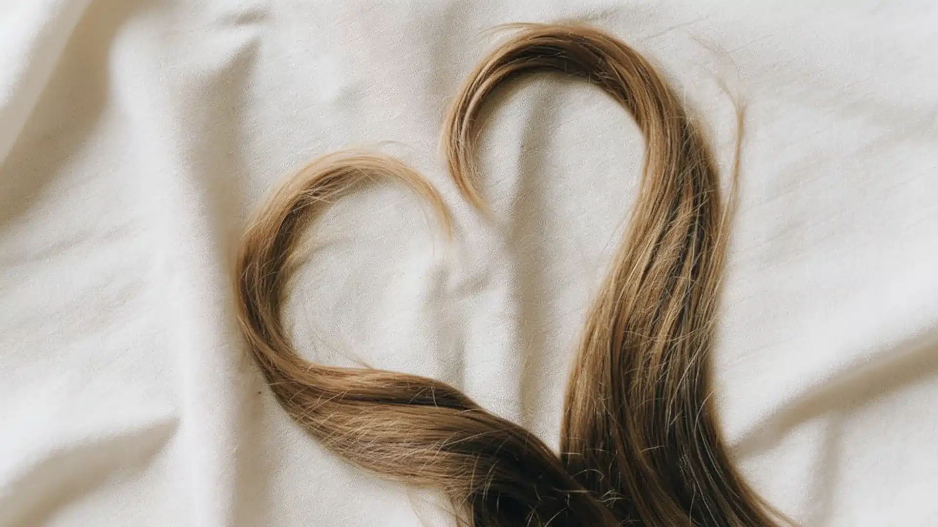 A heart-shaped piece of hair rests on a neatly made bed, showcasing a unique and artistic arrangement