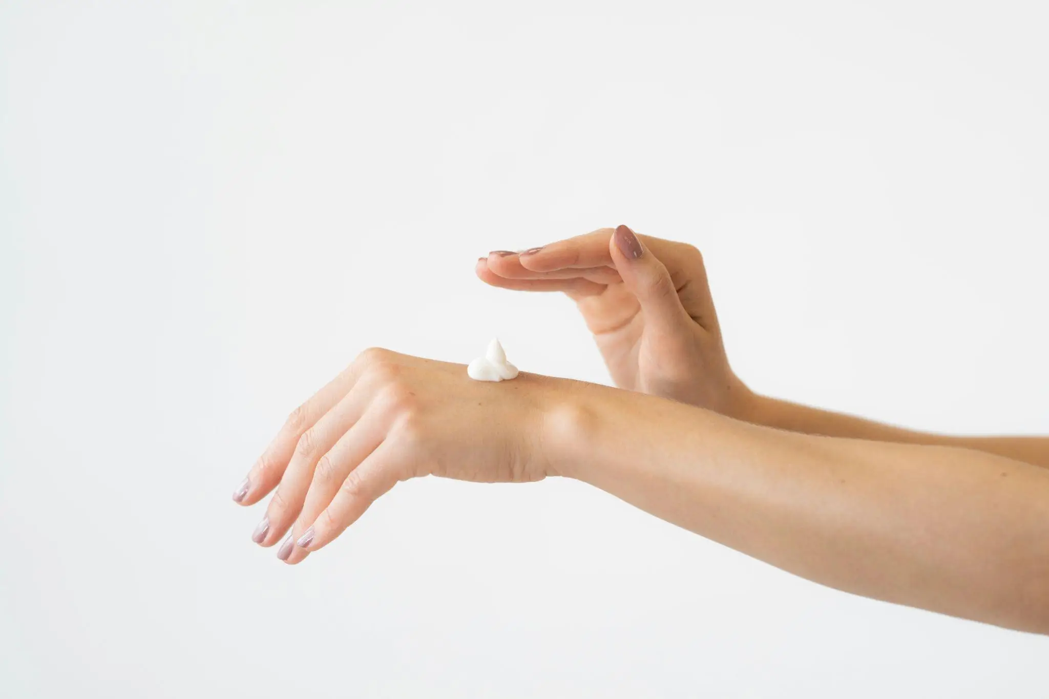 Applying moisturizer on hand with a dollop of cream against a white background