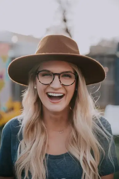 Smiling woman wearing glasses and brown hat outdoors with blurred background