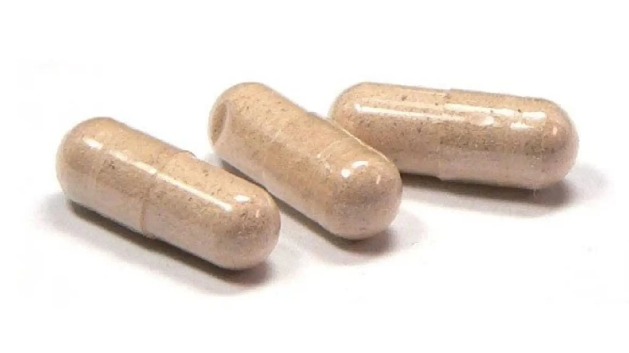 Three translucent beige capsules filled with powder of slippery elm rest on a white surface.