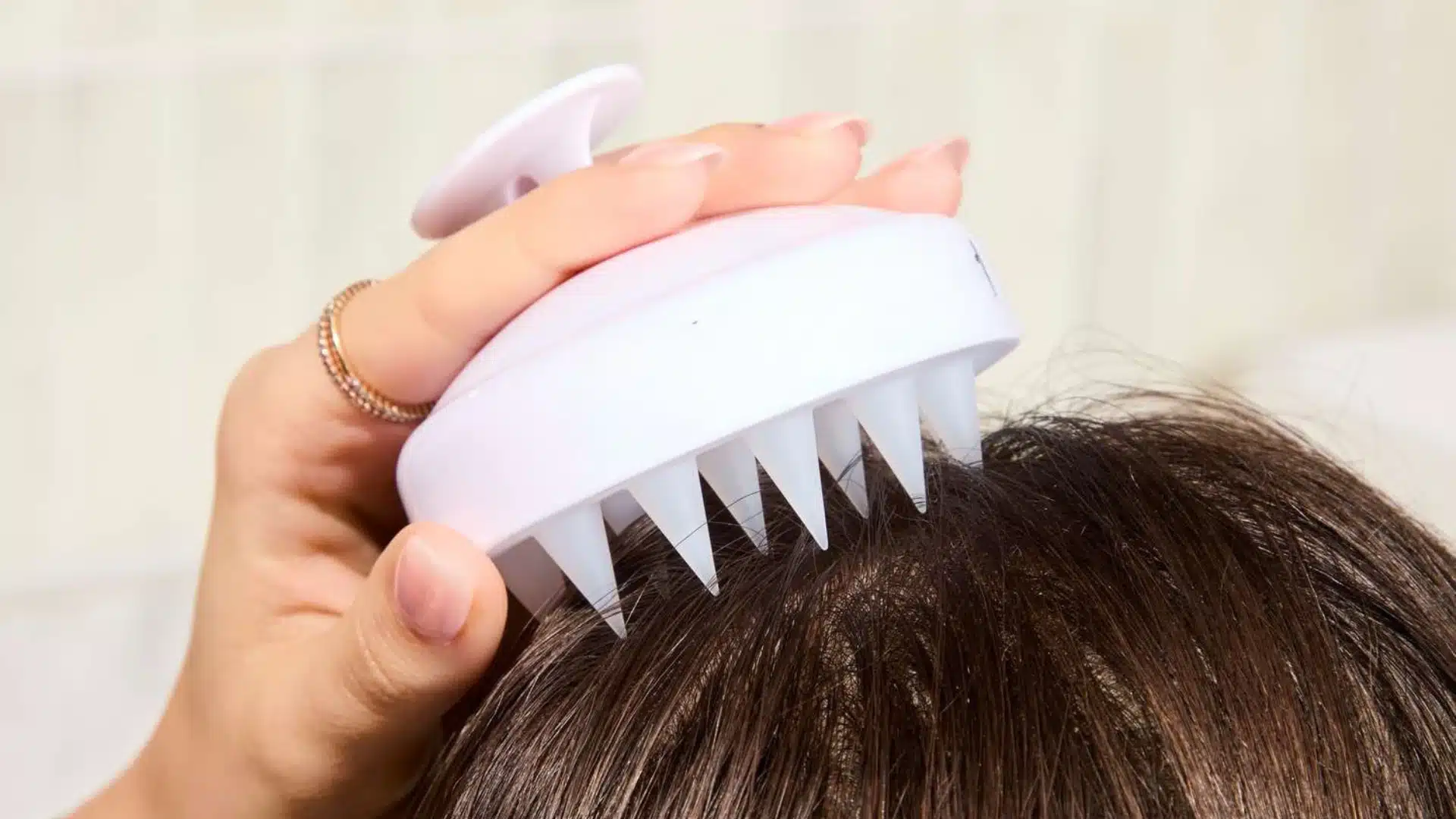 Close up of a silicone scalp massager gently massaging the scalp through parted hair