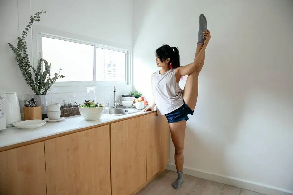 Person stretching leg in bright kitchen beside counter with salad bowl and plates