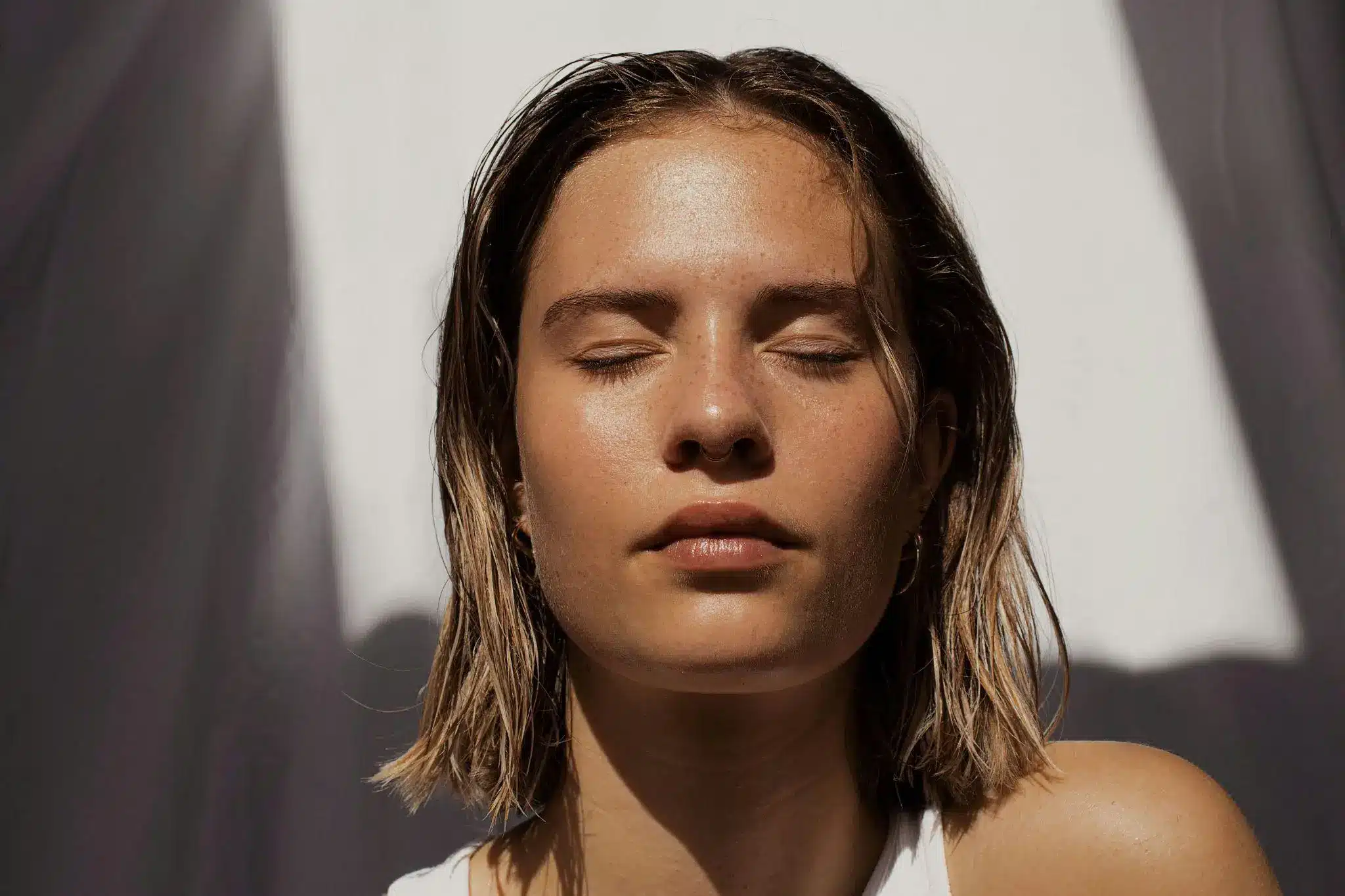 Woman with closed eyes under sunlight casting shadows in calm setting