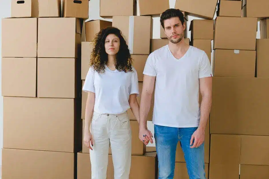 Couple holding hands in front of stacked moving boxes in bright room