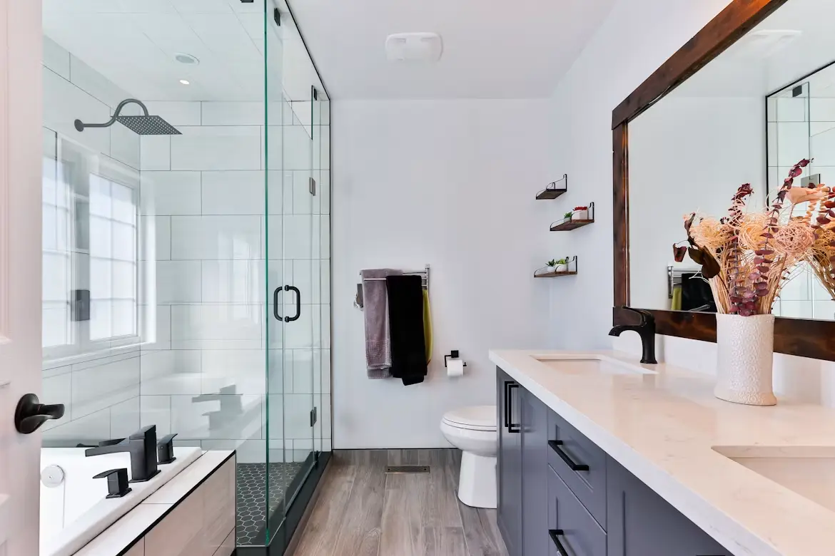 Modern bathroom with glass shower, double vanity and decorative vase under natural lighting