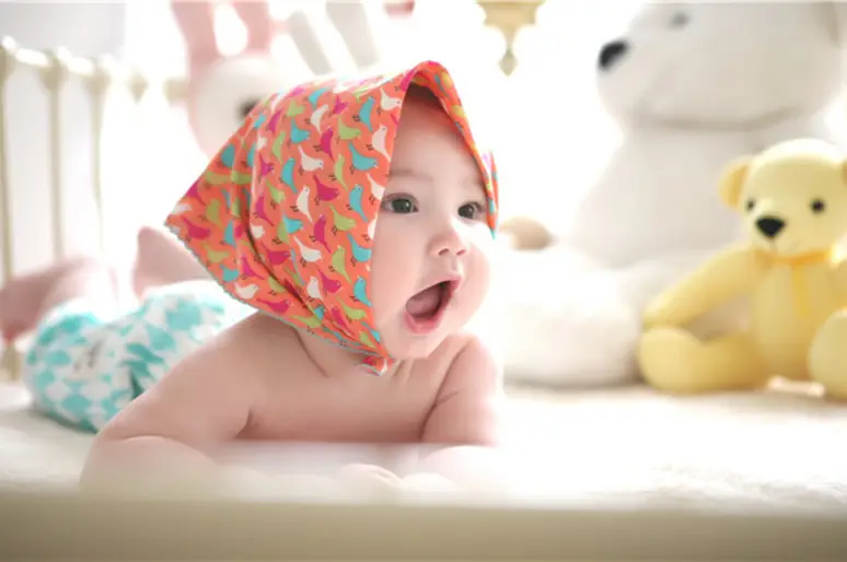 Baby lying on blanket with colorful headscarf in soft-lit nursery with stuffed animals