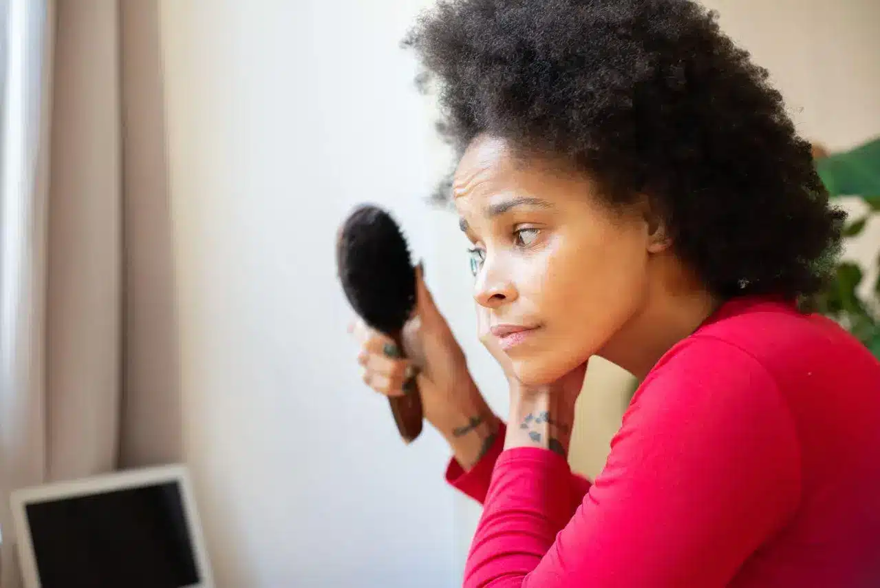 Person in red sweater holding hairbrush while looking in mirror indoors