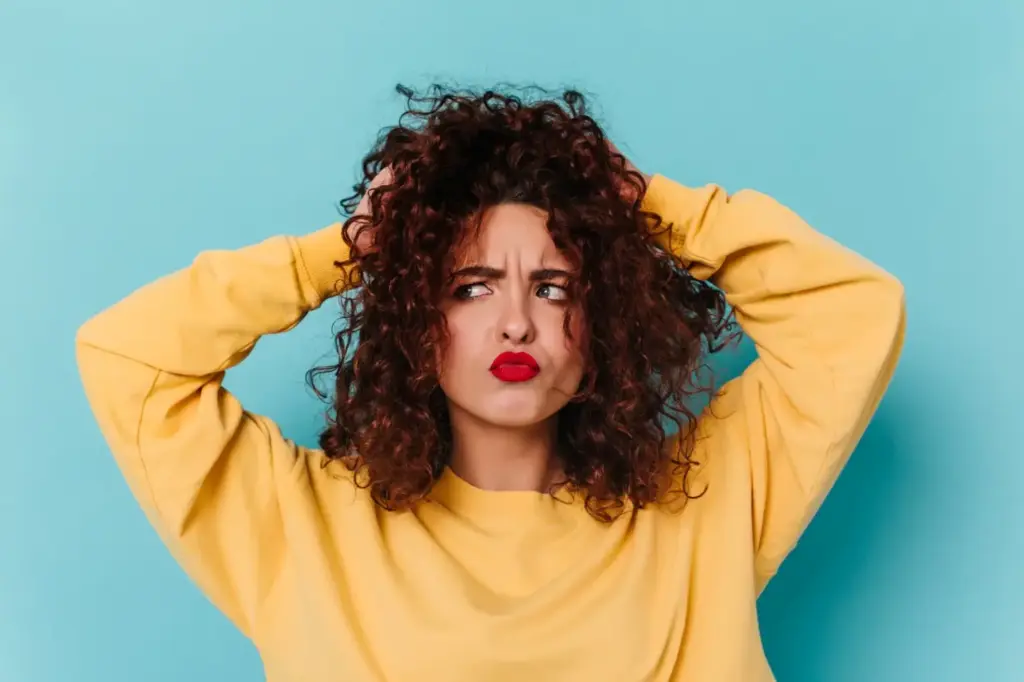 Curly-haired person in yellow sweater looking confused against blue background