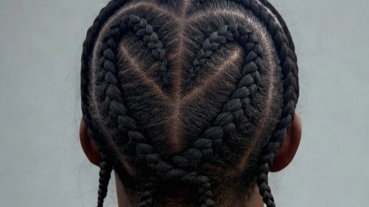 A man showcasing braids styled in a heart design, highlighting a unique and creative hairstyle.