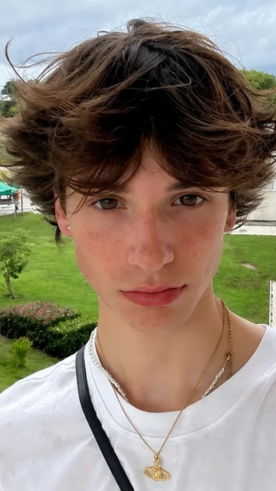 A young man in a white shirt and necklace, featuring a distinctive ice cream scoop-inspired hairstyle.