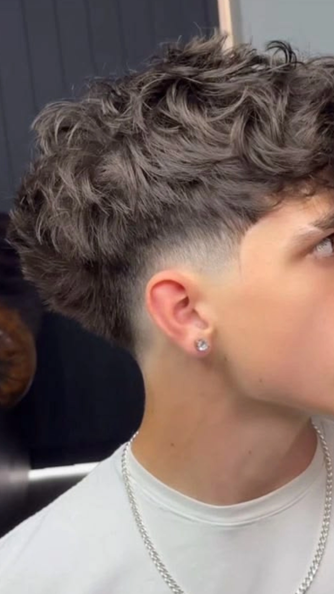 A young man with a curly taper fade haircut, showcasing short sides and longer curls on top.
