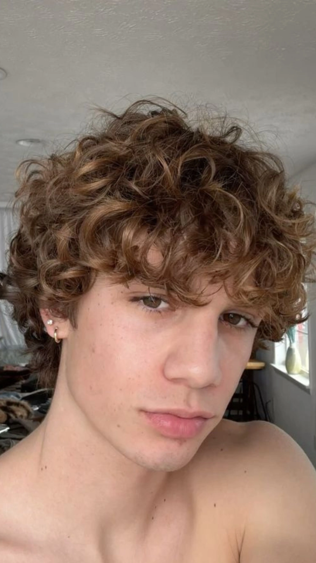 A young man with curly hair styled like ice cream, posing shirtless against a neutral background.
