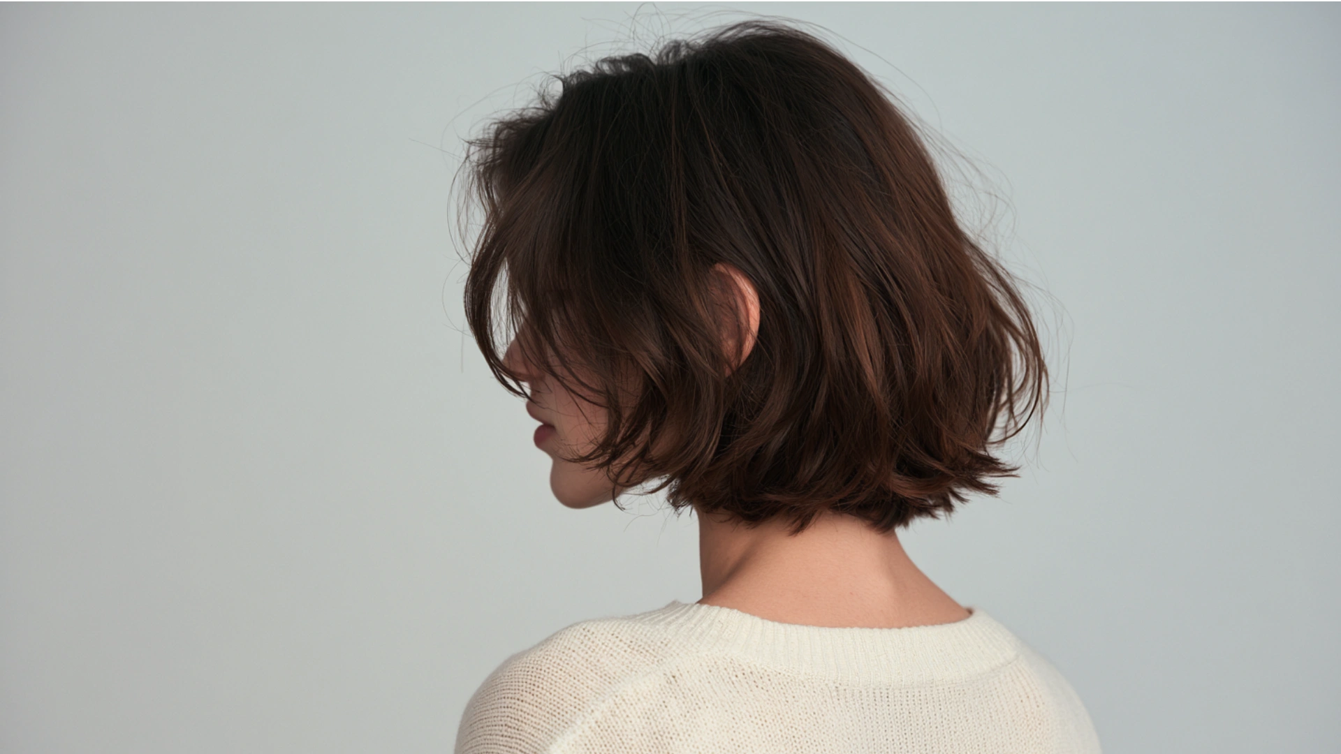 Back view of a woman with a stylish short brown bob haircut, emphasizing the hair's smooth texture and shape.