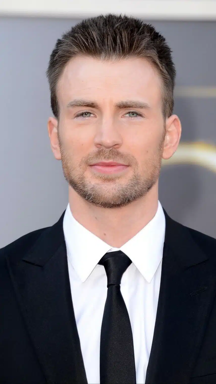 Chris Evans posing on the red carpet at the Oscars, wearing a classic tuxedo and smiling for the cameras.
