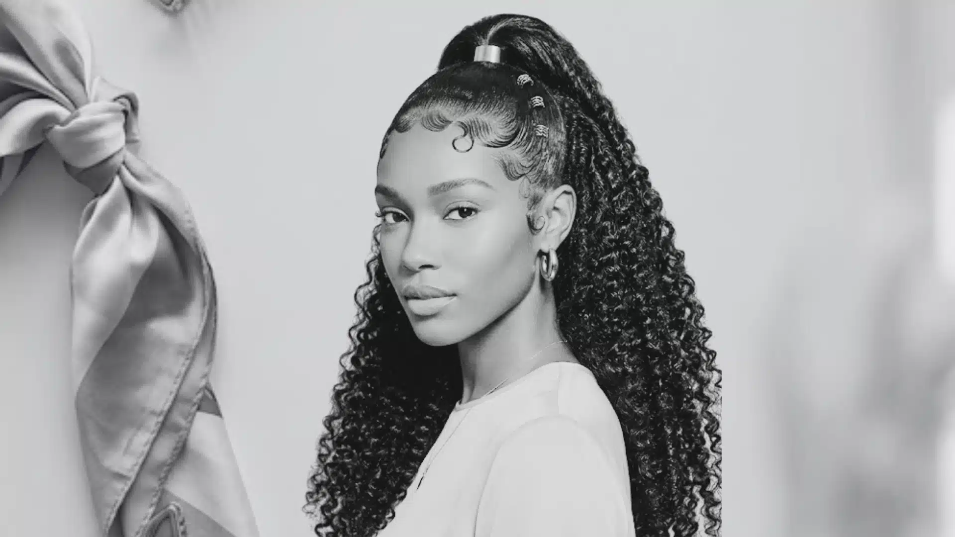 Black woman with sleek half-up ponytail, swooped edges, and long curly hair.