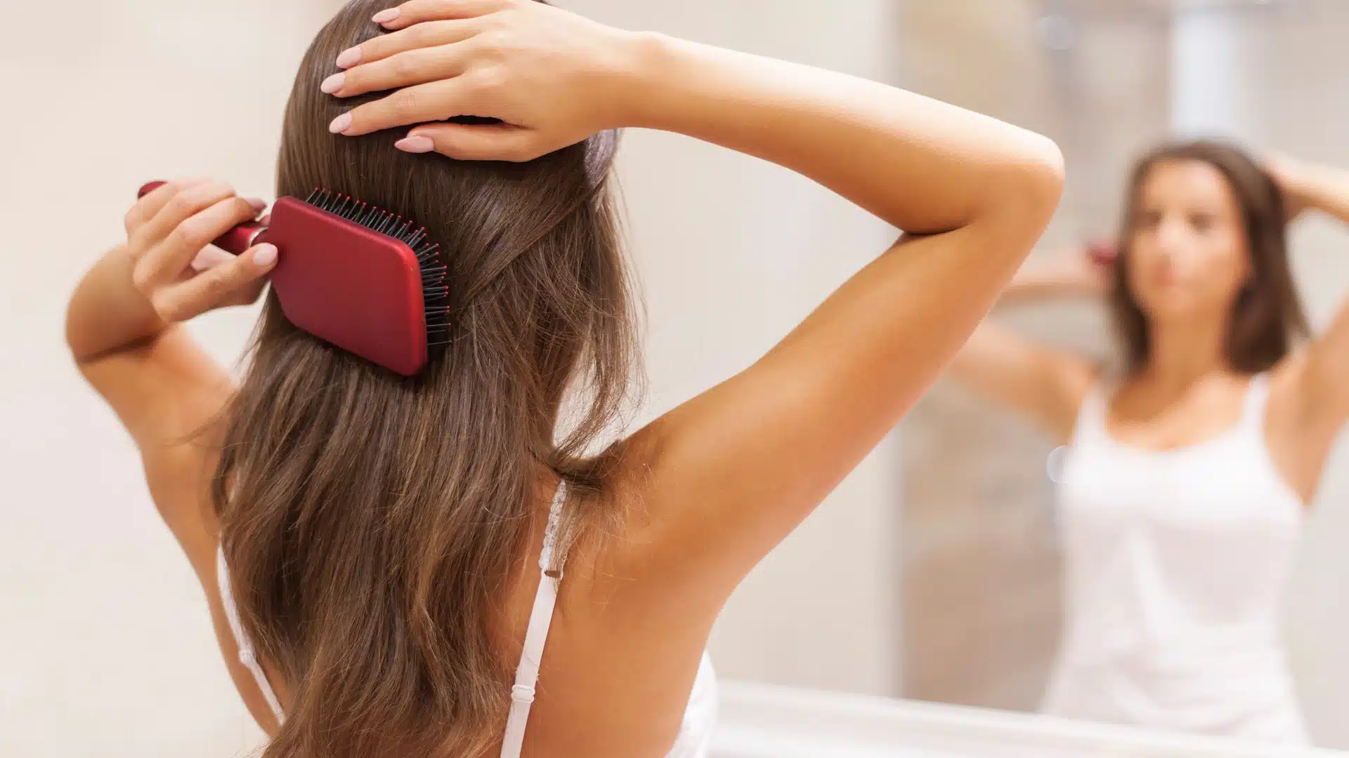 person brushing long brown hair with a paddle brush to support thicker looking hair and reduce breakage