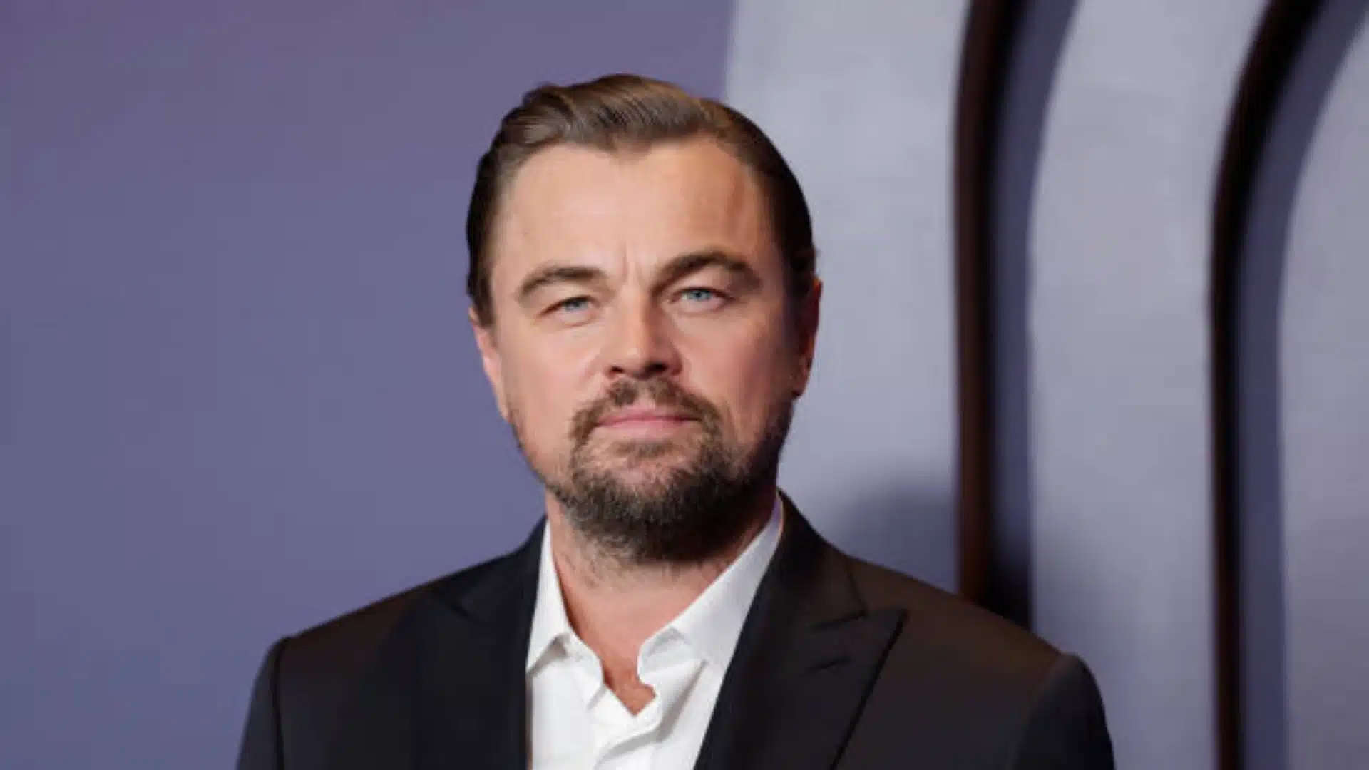 Medium length slicked back hairstyle with a neat side part and smooth polished finish paired with a short beard